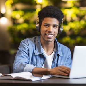 Cheerful teen guy with headset working with laptop